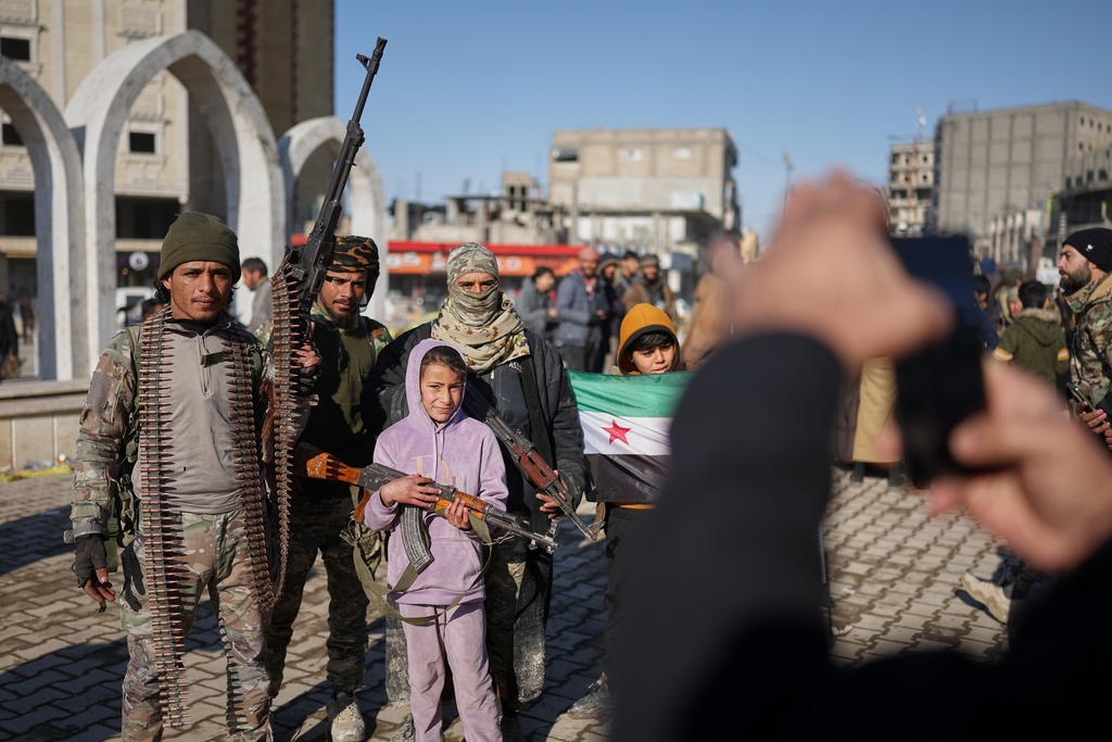 Tribal fighters pose for photographs with local children after Syrian government troops, supported by tribal forces, took control of Raqqa from the Syrian Democratic Forces (SDF) last Sunday at Al-Naeem roundabout in central Raqqa, northeastern Syria, Tuesday, Jan. 20, 2026. (AP Photo/Ghaith Alsayed)