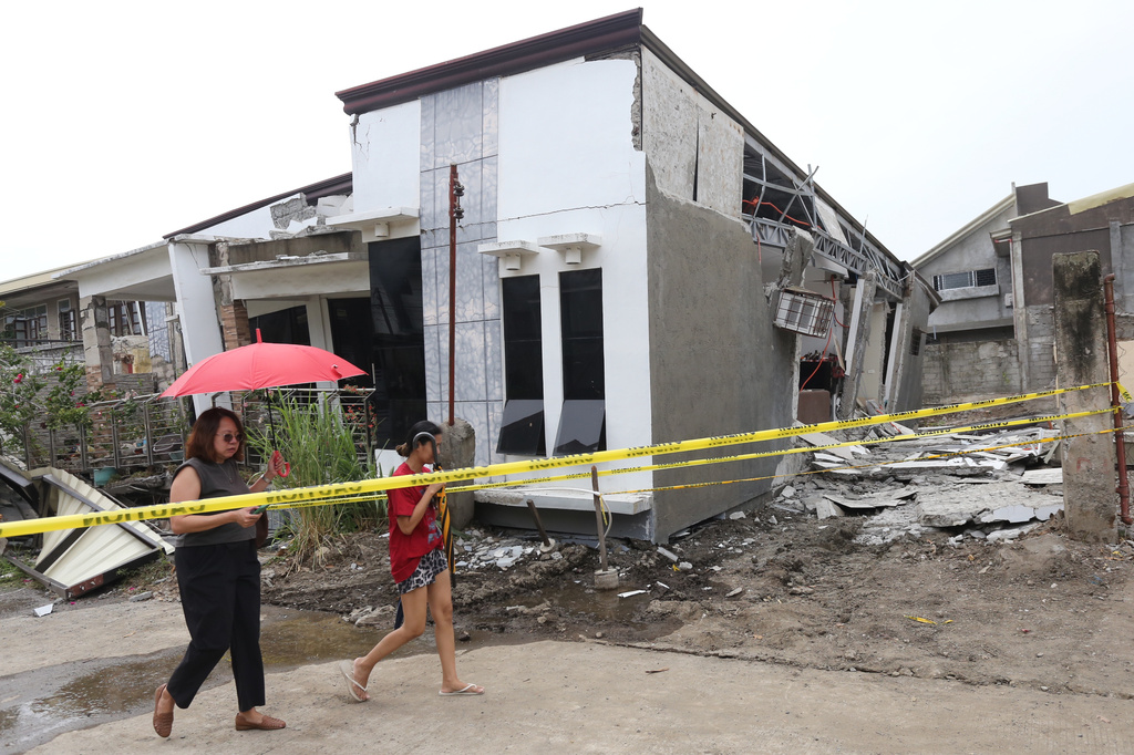 Two women walk past a damaged house after a strong earthquake in Davao City, southern Philippines on Friday Oct. 10, 2025. (AP Photo/Manman Dejeto)