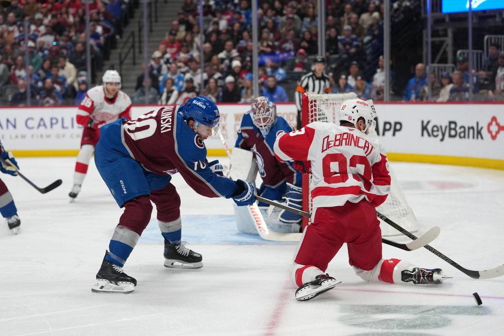 Detroit Red Wings right wing Alex DeBrincat, right, struggles to control the puck as Colorado Avalanche defenseman Sam Malinski, front left, covers in the second period of an NHL hockey game Monday, Feb. 2, 2026, in Denver. (AP Photo/David Zalubowski)