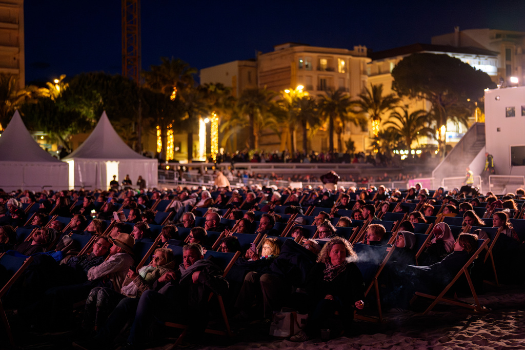 A woman checks her phone as people wait for the start of a movie on the beach during the 79th international film festival, Cannes, southern France, Friday, May 15, 2026. (AP Photo/Andreea Alexandru)