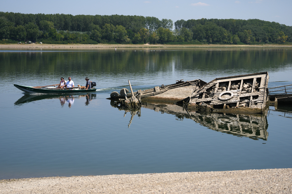 People watch the wreckage of a WWII German warship, emerged due to the drought, in front of Djerdap II, a large dam on the Danube River, between Romania and Serbia, near Prahovo, Serbia, Tuesday, Aug. 4, 2026. (AP Photo/Darko Vojinovic)