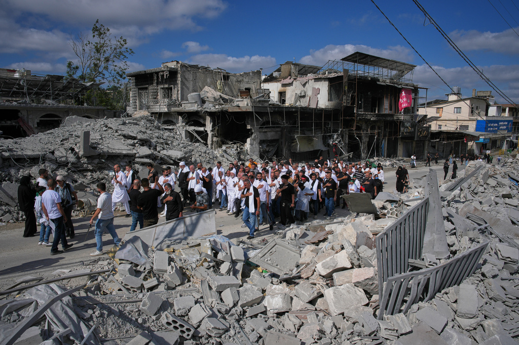 Lebanese Shiite men pass buildings destroyed by Israeli strikes during an Ashoura procession, when Shiites commemorate the martyrdom of Imam Hussein, the grandson of the Prophet Muhammad, in Nabatiyeh, southern Lebanon, Friday, June 26, 2026. (AP Photo/Hassan Ammar)