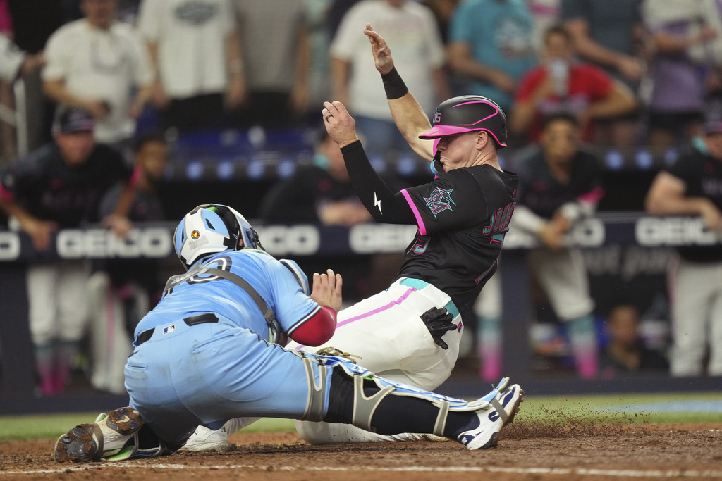 Miami Marlins' Troy Johnston, left, gets tagged out by Toronto Blue Jays catcher Alejandro Kirk (30) during the seventh inning of a baseball game, Saturday, Aug. 23, 2025, in Miami. (AP Photo/Jim Rassol)