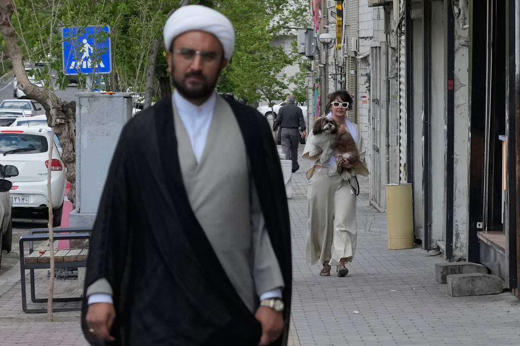 A woman carries her dog as a cleric walks on a sidewalk in Tehran, Iran, Tuesday, April 21, 2026. (AP Photo/Vahid Salemi)
