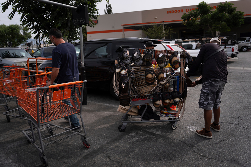 FILE - Vendor Felix, right, shows merchandise to a man as a shopper returns a cart in the parking lot of a Home Depot in the Van Nuys section of Los Angeles, Aug. 28, 2025. (AP Photo/Jae C. Hong, File)