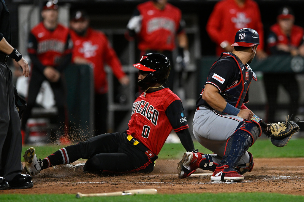 Chicago White Sox's Luisangel Acuna (0) scores on an Andrew Benintendi sacrifice fly while Washington Nationals catcher Drew Millas, right, attempts to apply a tag during the seventh inning of a baseball game in Chicago, Friday, April 24, 2026. (AP Photo/Paul Beaty)