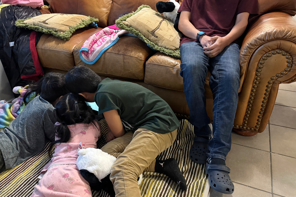 A boy sits on the couch of a Minneapolis safe house Friday, Jan. 16, 2026, as his younger siblings and niece play on the floor beside him after they fled their home because they were sought by federal immigration enforcement agents. (AP Photo/Jack Brook)