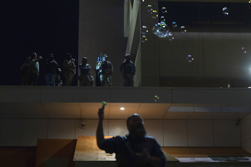 A protester makes bubbles as officials watch from a ledge at a U.S. Immigration and Customs Enforcement facility on Thursday, Oct. 2, 2025, in Portland, Ore. (AP Photo/Jenny Kane)