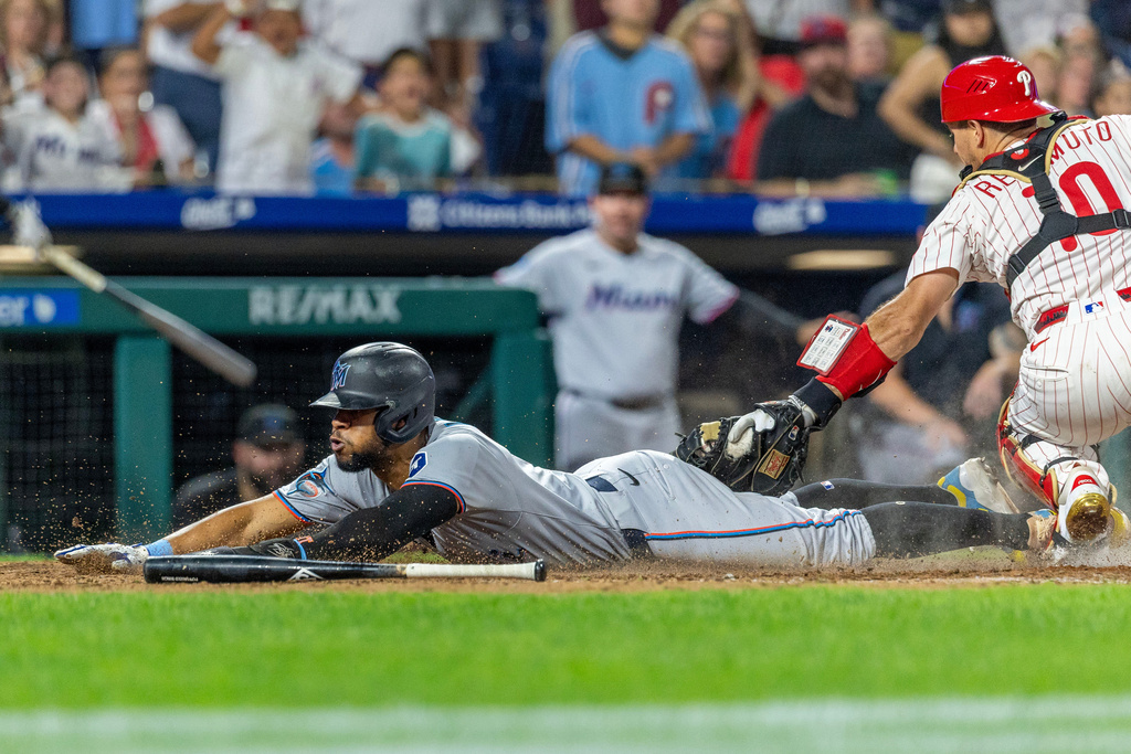 Miami Marlins' Otto Lopez, left, scores before Philadelphia Phillies catcher J.T. Realmuto, right, can make the tag during the eighth inning of a baseball game, Tuesday, Sept. 23, 2025, in Philadelphia. (AP Photo/Laurence Kesterson)
