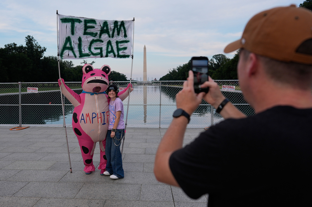 Brian Van, right, takes a photo of Carina Miller, center, with a member of "Team Algae" at the Lincoln Memorial Reflecting Pool Thursday, June 25, 2026, in Washington. (AP Photo/Carolyn Kaster)