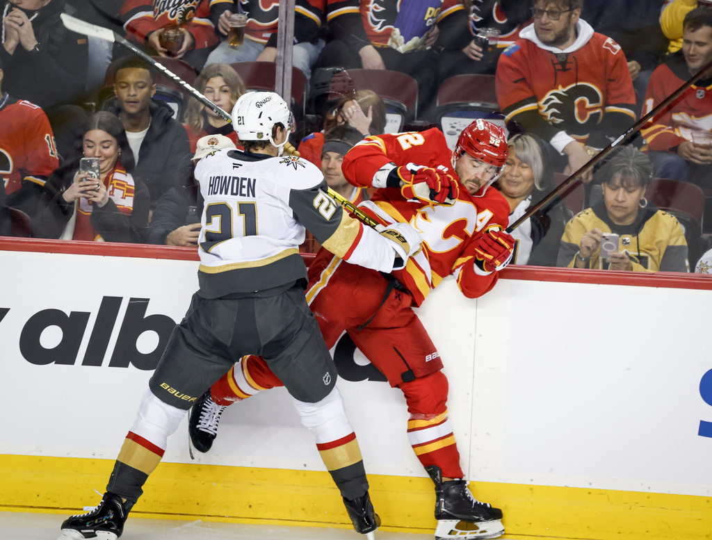 Vegas Golden Knights' Brett Howden, left, checks Calgary Flames' MacKenzie Weegar, right, during first-period NHL hockey game action in Calgary, Saturday, Dec. 20, 2025. (Jeff McIntosh/The Canadian Press via AP)