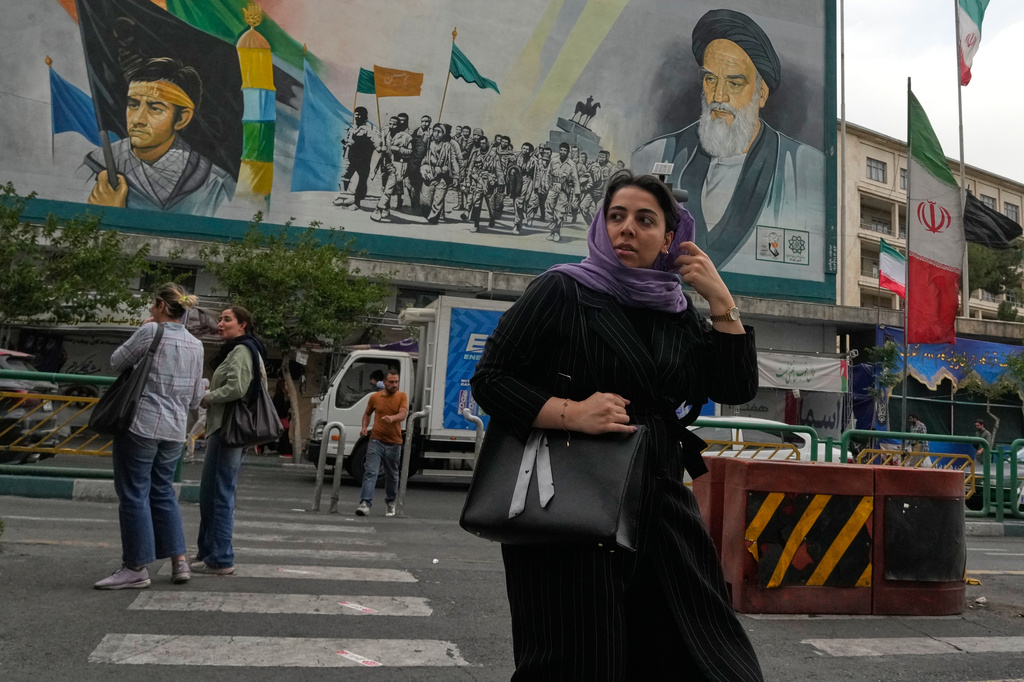 A woman crosses a street in front of a painting of the late Iranian revolutionary founder Ayatollah Khomeini and paramilitary Basij forces in downtown Tehran, Iran, Sunday, May 24, 2026. (AP Photo/Vahid Salemi)