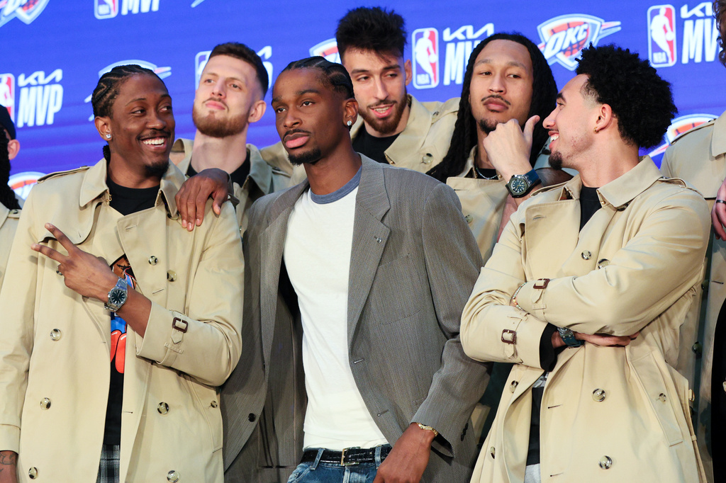 Oklahoma City Thunder guard Shai Gilgeous-Alexander, center, poses with teammates Jalen Williams, left, Isaiah Hartenstein, second from left, Chet Holmgren, center back, Jaylin Williams, second from right, and Jared McCain, right, in Burberry trench coats bought by Gilgeous-Alexander during a news conference after he was named the NBA basketball MVP, Sunday, May 17, 2026, in Oklahoma City. (AP Photo/Nate Billings)