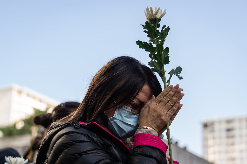 People holds flower and prays near the scene after the deadly fire that started Wednesday at Wang Fuk Court, a residential estate in the Tai Po district of Hong Kong's New Territories, Saturday Nov. 29, 2025. (AP Photo/Chan Long Hei)