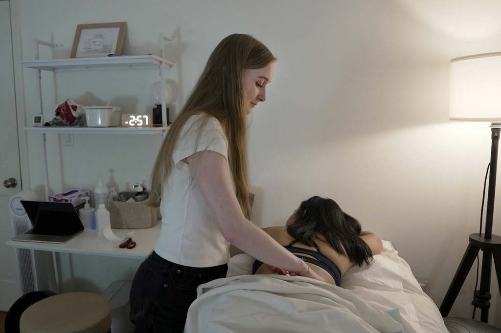 Zoë Armstrong, an endometriosis patient, rests during her pelvic floor physical therapy appointment with physical therapist Emma Codman, standing, in New York, Friday, Aug. 14, 2026. (AP Photo/Shelby Lum)