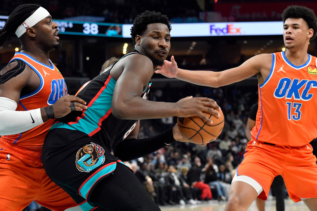 Memphis Grizzlies forward Jaren Jackson Jr. (8) handles the ball between Oklahoma City Thunder guard Luguentz Dort, left, and forward Ousmane Dieng (13) in the first half of an NBA basketball game Friday, Jan. 9, 2026, in Memphis, Tenn. (AP Photo/Brandon Dill)