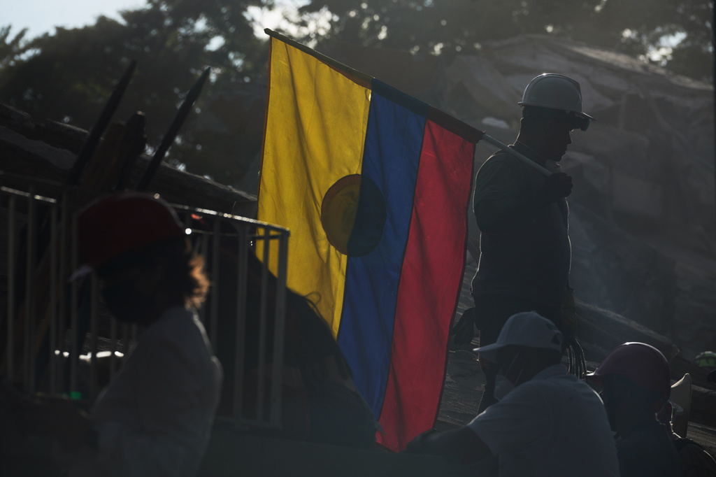 A firefighter working on rescue efforts holds a Colombian flag amid the rubble three days after an earthquake struck Cali, Colombia, Thursday, Aug. 13, 2026. (AP Photo/Ivan Valencia)
