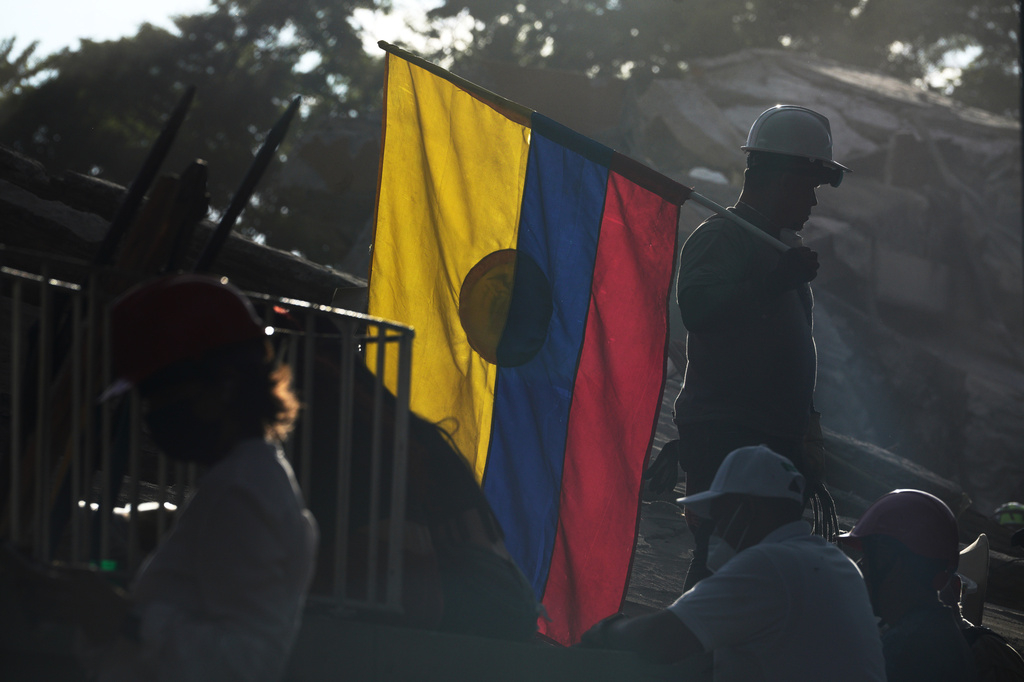 A firefighter working on rescue efforts holds a Colombian flag amid the rubble three days after an earthquake struck Cali, Colombia, Thursday, Aug. 13, 2026. (AP Photo/Ivan Valencia)