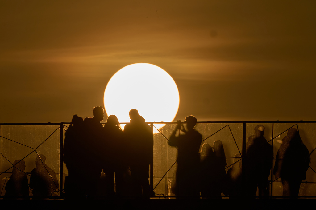 People watch and take photos during sunset in Moscow, Thursday, March 12, 2026. (AP Photo/Alexander Zemlianichenko)