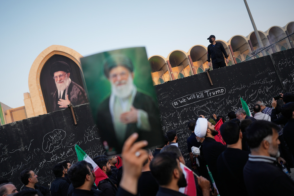A mourner holds a portrait of the late Iranian Supreme Leader Ayatollah Ali Khamenei as he walks past a wall bearing messages, including one in English that reads "We will kill Trump," during the funeral ceremonies for Khamenei and members of his family at the Imam Khomeini Mosalla Grand Mosque in Tehran, Iran, Saturday, July 4, 2026. (AP Photo/Altaf Qadri)
