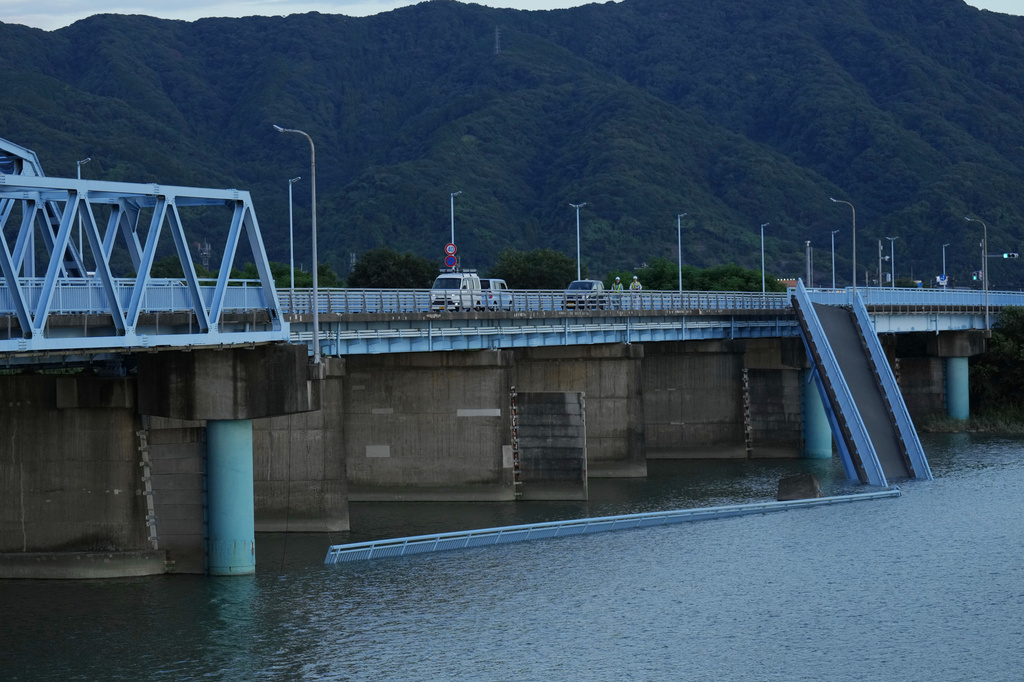Men walking on a car lane of a bridge inspect a damaged bridge built abreast for pedestrians in Yatsushiro, southwestern Japan, Wednesday, July 29, 2026, the day after an earthquake hit the area. (AP Photo/Hiro Komae)