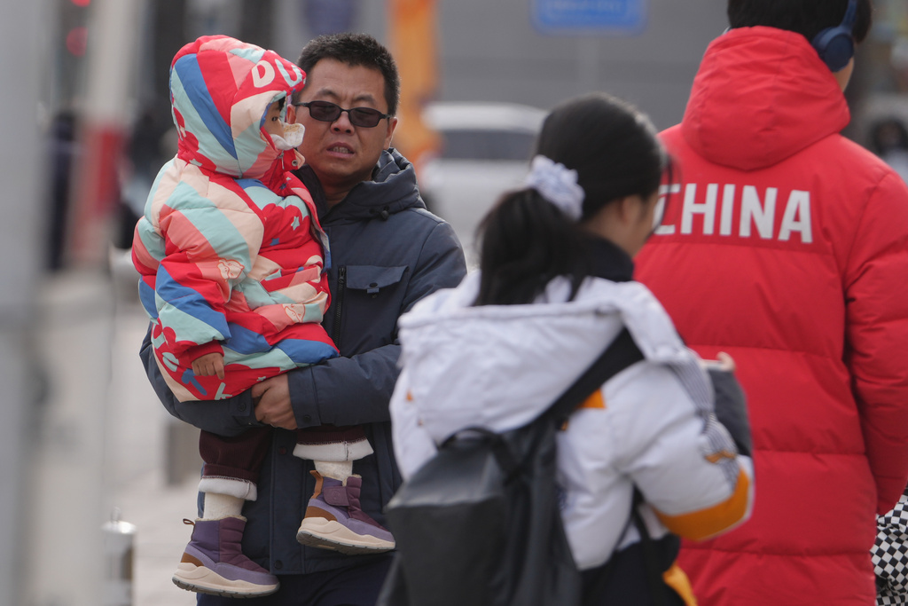 A man carries a toddler along a street in Beijing, Monday, Jan. 19, 2026. (AP Photo/Andy Wong)