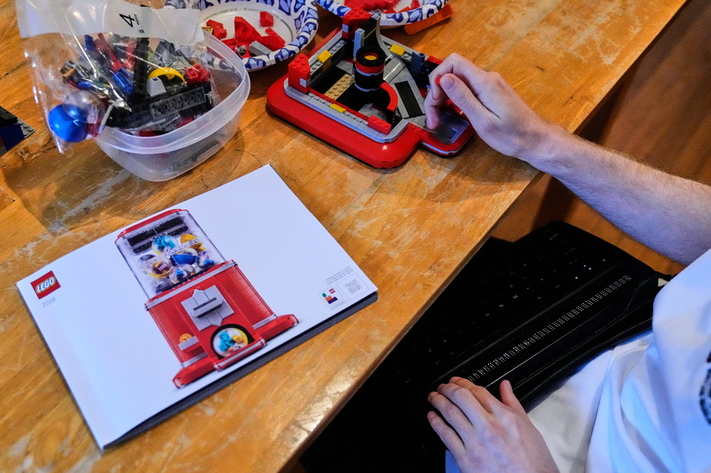 Matthew Shifrin, the founder of Bricks for the Blind, reads from a braille terminal while building a LEGO gum ball machine at his family's home, Friday, March 20, 2026, in Newton, Mass. (AP Photo/Charles Krupa)