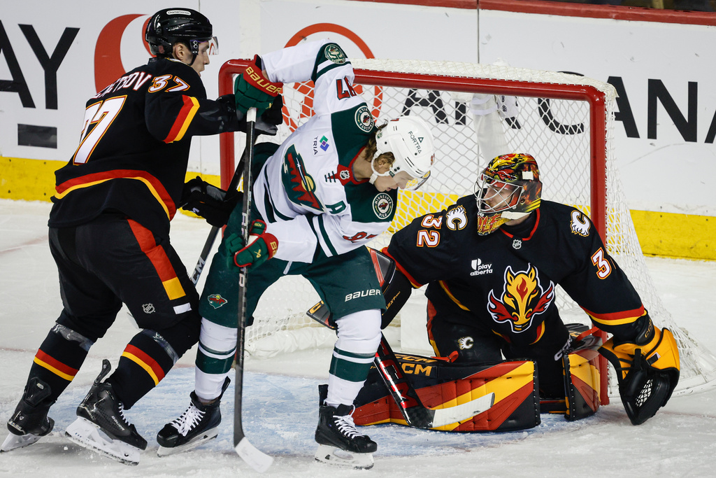 Minnesota Wild's Kirill Kaprizov, centre, is checked by Calgary Flames' Yan Kuznetsov, left, in front of goalie Dustin Wolf, during the first period of an NHL hockey game in Calgary, Alberta, Thursday, Dec. 4, 2025. (Jeff McIntosh/The Canadian Press via AP)