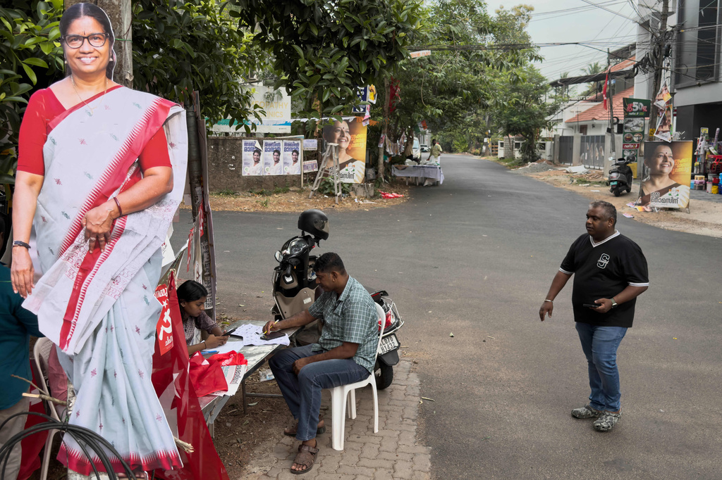 A voter, right, arrives to check his name at an assistance booth set up by party workers as a candidate's cut out photo is displayed on left during the Kerala state election in Kochi, India, Thursday, April 9, 2026. (AP Photo/ R S Iyer)