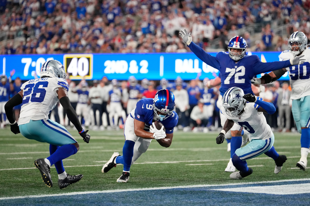 New York Giants tight end Isaiah Likely (9), with teammate guard Jermaine Eluemunor (72) reacting, scores a touchdown run between Dallas Cowboys cornerback Daron Bland (26) and linebacker DeMarvion Overshown (0 ) during the second half of an NFL football game Sunday, Sept. 13, 2026, in East Rutherford, N.J. (AP Photo/Yuki Iwamura)