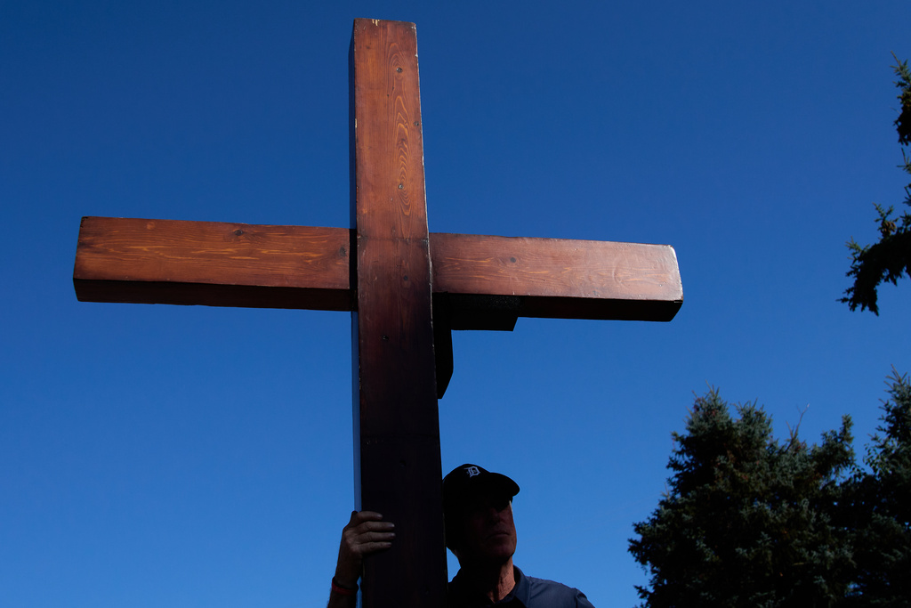 Dan Beazley, of Northville, carries a homemade cross to The Church of Jesus Christ of Latter-day Saints in Grand Blanc Township, Mich., Tuesday, Sept. 30, 2025, after a man rammed his vehicle into the building before opening fire and setting the building ablaze Sunday morning. (AP Photo/Ryan Sun)