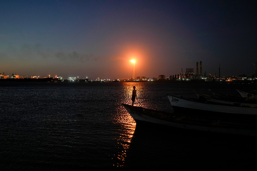 A boy stands on a fishing boat with the Cardon refinery in the background in Punta Cardon, Venezuela, Wednesday, Jan. 14, 2026. (AP Photo/Matias Delacroix)