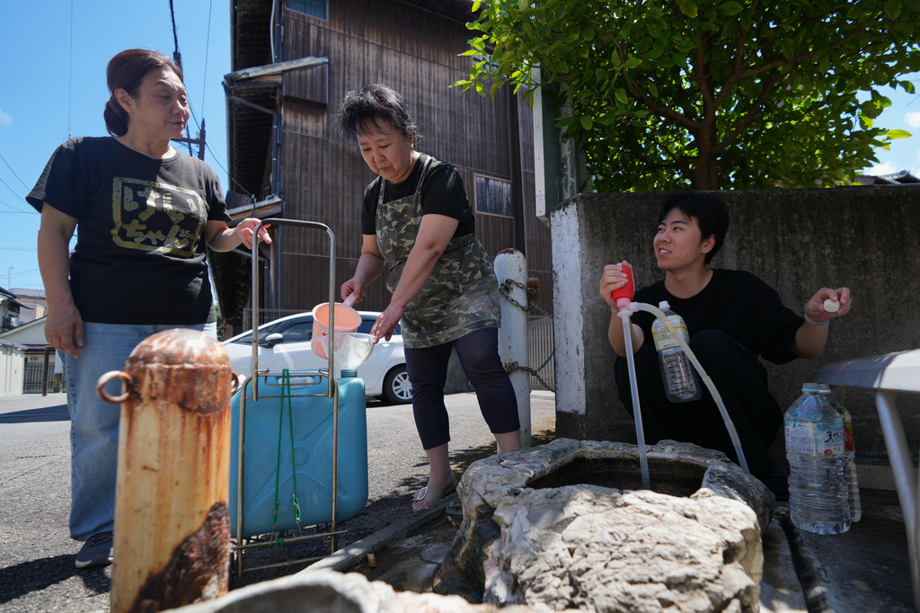 A local woman chats with others as they collect hot spring water in Yatsushiro, southern Japan, Friday, July 31, 2026, three days after an earthquake hit the area. (AP Photo/Hiro Komae)
