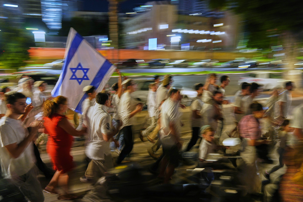 Jewish revelers dance and hold up the Torah as they celebrate the holiday of Simchat Torah next to the plaza known as hostages square, in Tel Aviv, Israel, Tuesday, Oct. 14, 2025. (AP Photo/Francisco Seco)