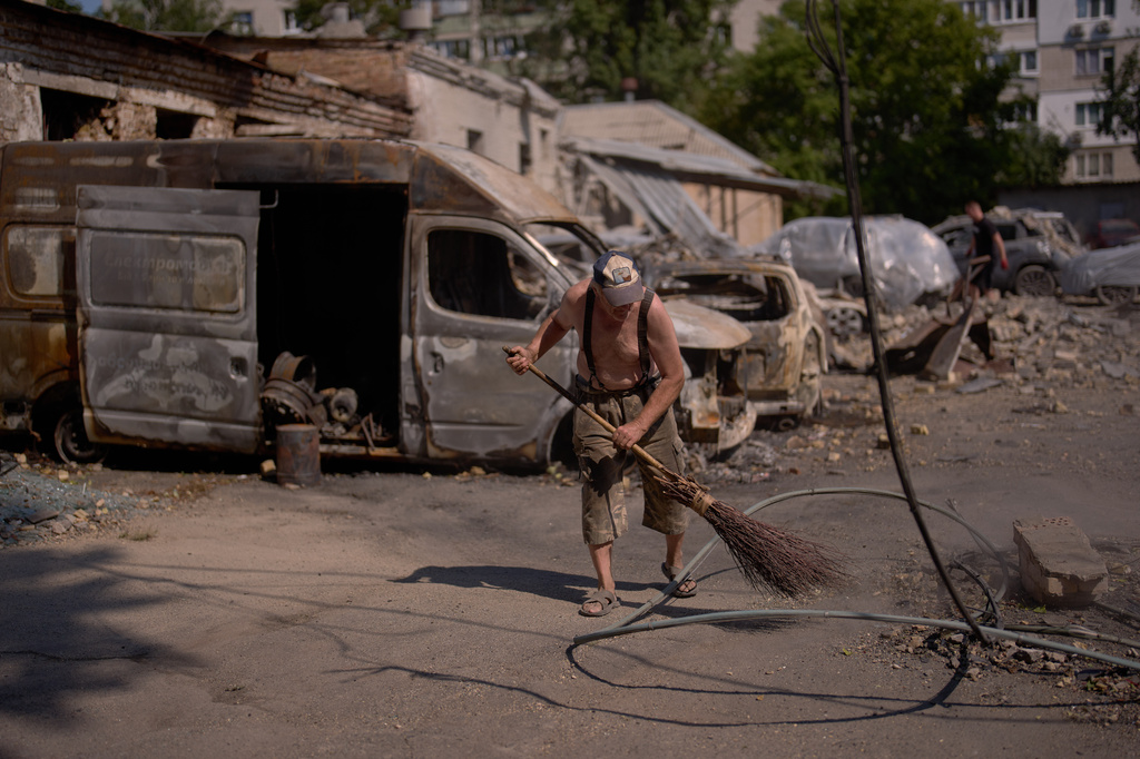 A local resident removes scattered debris next to destroyed vehicles the day after a Russian missile and drone attack in Kyiv, Friday, Aug. 21, 2026. (AP Photo/Francisco Seco)