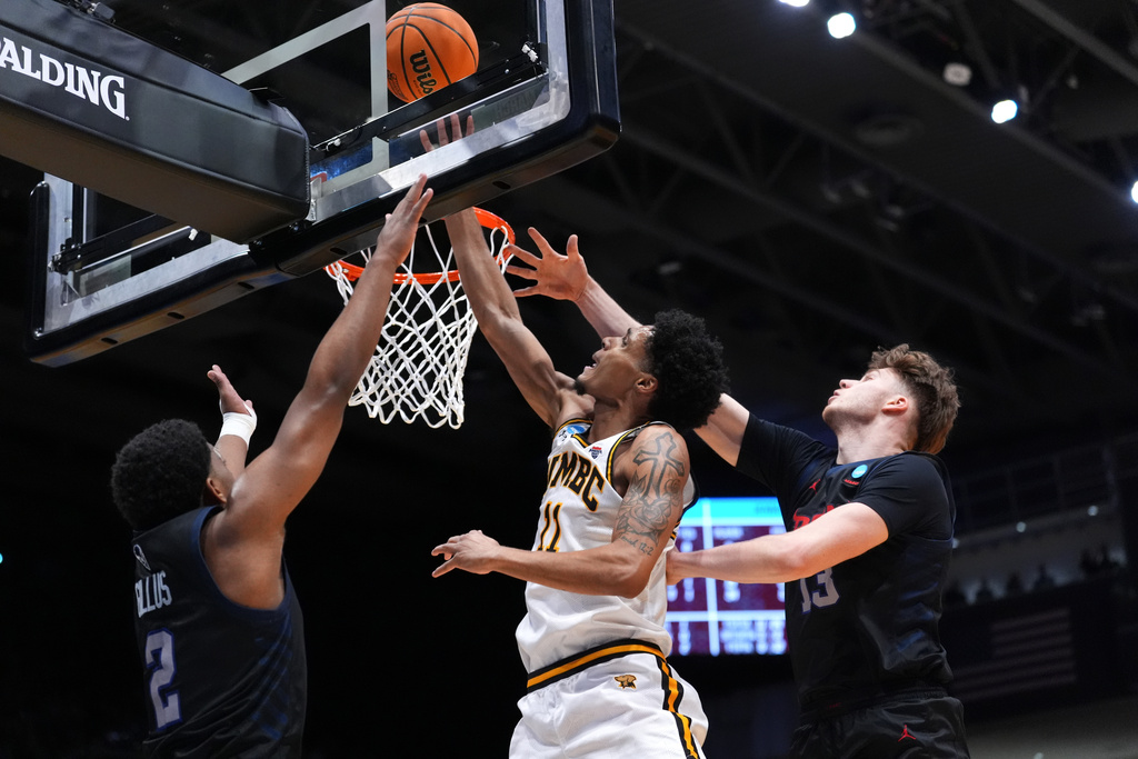 UMBC forward Caden Diggs (11), center, scores at the basket as Howard guard Cam Gillus (2), left, and center Danas Kazakevicius (13), right, defend during the first half in a First Four college basketball game in the NCAA Tournament, Tuesday, March 17, 2026, in Dayton, Ohio. (AP Photo/Kareem Elgazzar)