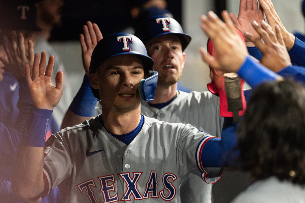 Texas Rangers' Michael Helman, front and Billy McKinney, rear, are greeted by their teammates after scoring on an RBI single by Cody Freeman during the seventh inning of a baseball game, Friday, Sept. 26, 2025, in Cleveland. (AP Photo/Phil Long)