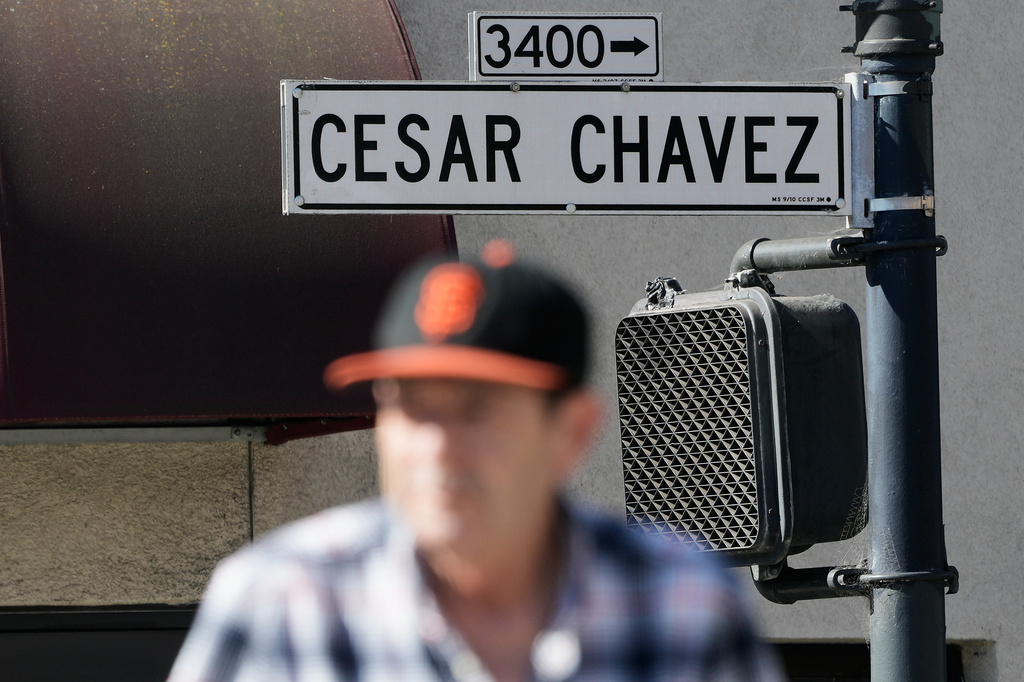 A pedestrian walks below a César Chavez Street sign in San Francisco, Wednesday, March 18, 2026. (AP Photo/Jeff Chiu)