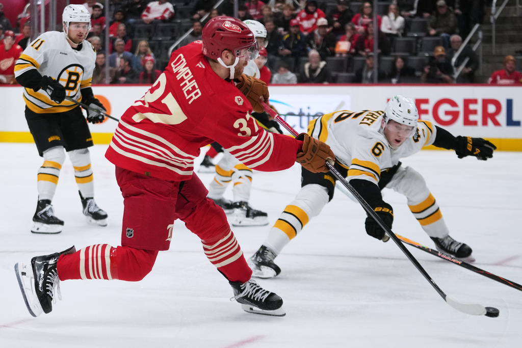 Detroit Red Wings left wing J.T. Compher (37) shoots a Boston Bruins defenseman Mason Lohrei (6) defends in the second period of an NHL hockey game Tuesday, Dec. 2, 2025, in Detroit. (AP Photo/Paul Sancya)