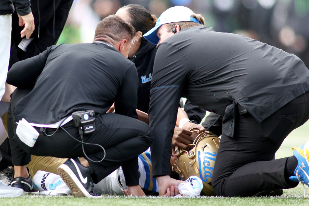 UCLA quarterback Nico Iamaleava (9) is examined by head coach Bob Chesney, left, and medical staff during the first half of an NCAA college football game against Oregon, Saturday, Oct. 10, 2026, in Eugene, Ore. (AP Photo/Lydia Ely)