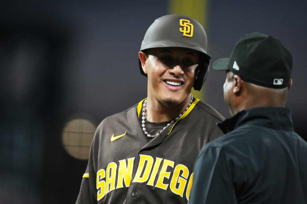 San Diego Padres' Manny Machado, back, jokes with first base umpire Alan Porter in the sixth inning of a baseball game against the Colorado Rockies Tuesday, April 21, 2026, in Denver. (AP Photo/David Zalubowski)
