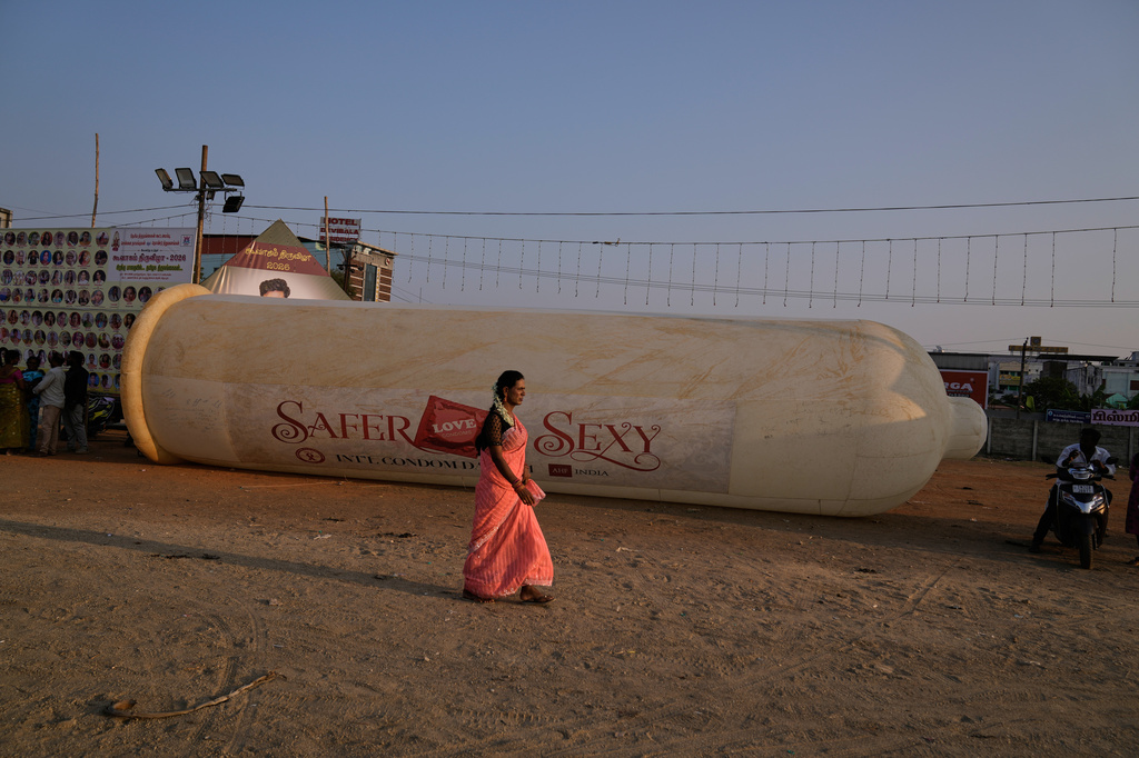 A transgender beauty pageant participant walks past a large condom replica displayed at a health awareness event during the Koovagam festival in Villupuram, Tamil Nadu, India. Sunday, April 26, 2026. (AP Photo/Mahesh Kumar A.)