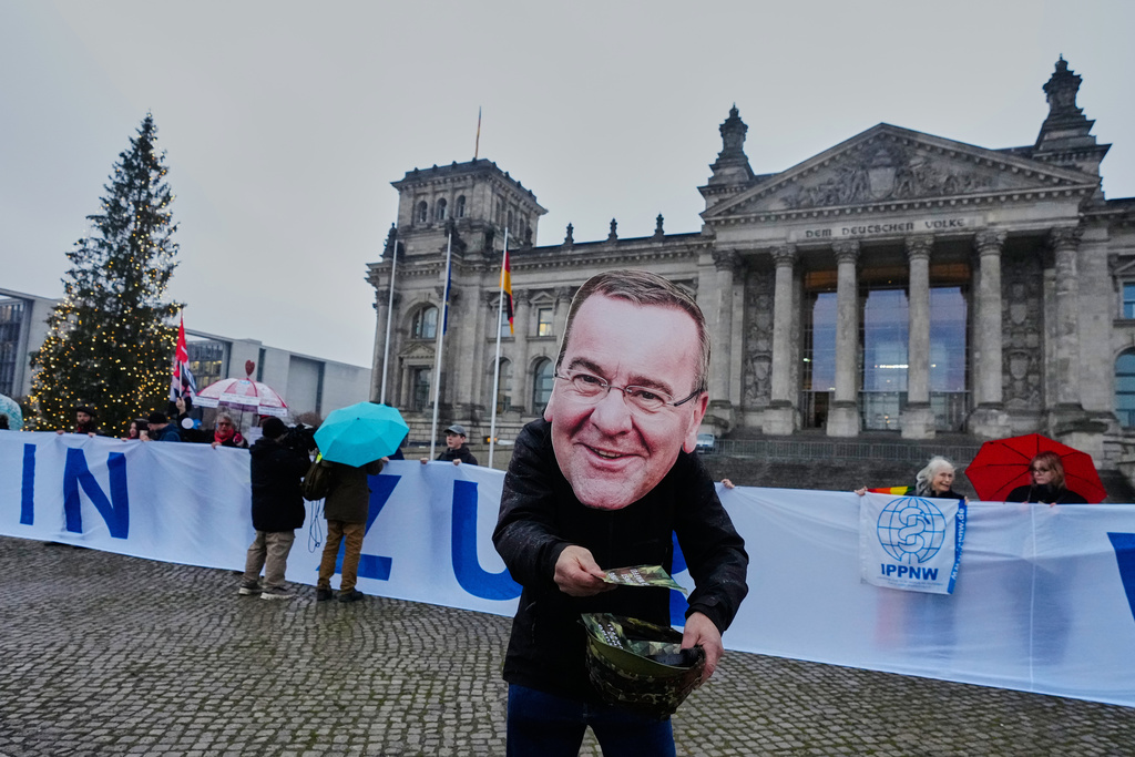A demonstration with the mask of German Defence Minister Boris Pistorius attends a protest against the planned possibility of compulsory service in front of the German parliament in Berlin, Germany , Friday, Dec. 5, 2025. (AP Photo/Markus Schreiber)