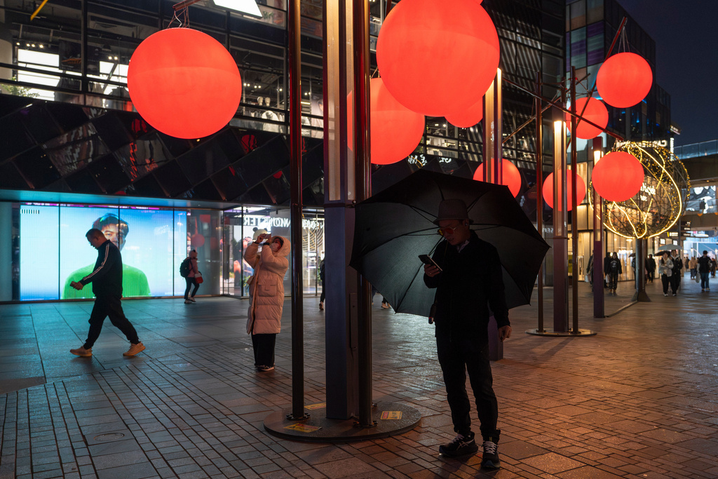 A man checks his phone near decorative red balls at the Taikoo Li Sanlitun mall in Beijing, Wednesday, Oct. 22, 2025. (AP Photo/Ng Han Guan)