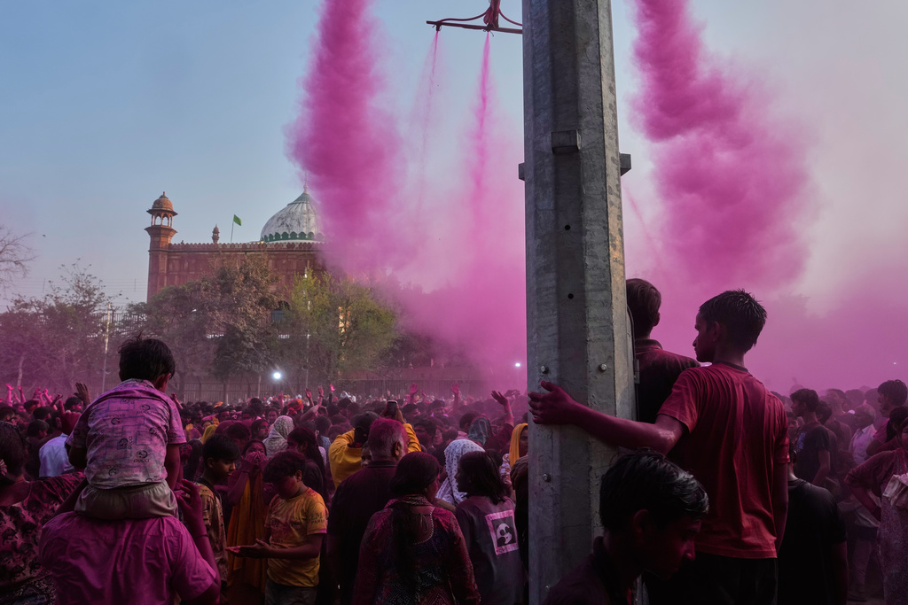 Children watch as revelers dance under colored water and powder sprayed from above at the Shri Krishna Janmabhoomi Temple complex during Holi festival celebrations in Mathura, India, on Feb. 27, 2026. (AP Photo/Manish Swarup)