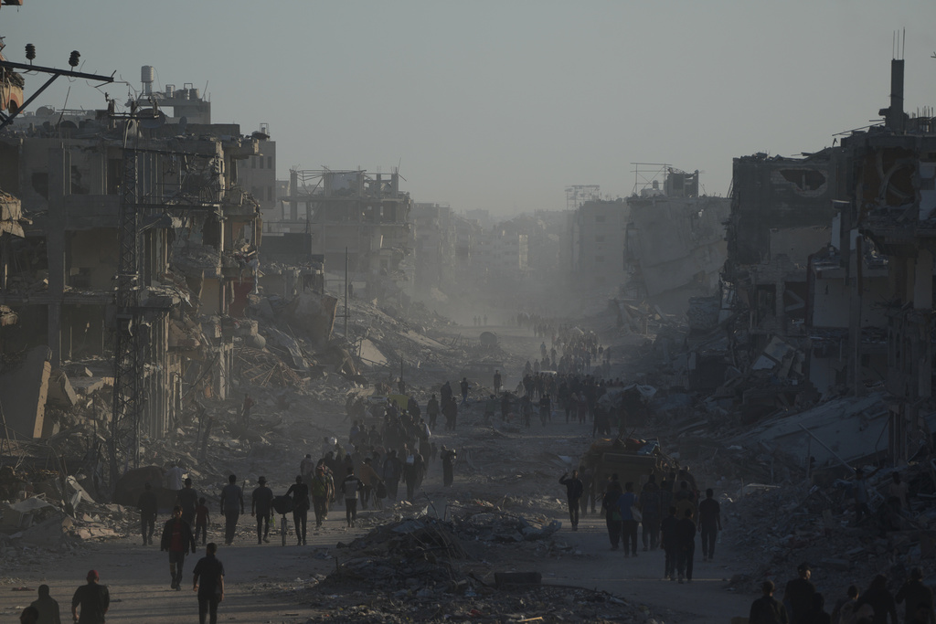 Displaced Palestinians carry their belongings as they walk along the heavily damaged Al-Jalaa Street in Gaza City, Saturday, Oct. 11, 2025, after Israel and Hamas agreed to a pause in their war and the release of the remaining hostages. (AP Photo/Abdel Kareem Hana)