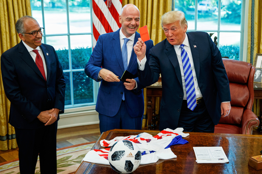 FILE - President Donald Trump holds up a red card during a meeting with FIFA president Gianni Infantino, center, and United States Soccer Federation president Carlos Cordeiro, left, in the Oval Office of the White House, Aug. 28, 2018, in Washington. (AP Photo/Evan Vucci, File)