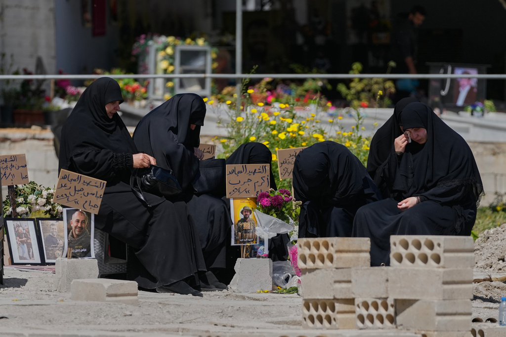 Relatives of a Hezbollah fighter mourn on his grave at a cemetery where civilians and Hezbollah fighters killed in Israeli airstrikes are temporarily buried in the southern port city of Sidon, Lebanon, Tuesday, April 14, 2026. (AP Photo/Mohammed Zaatari)