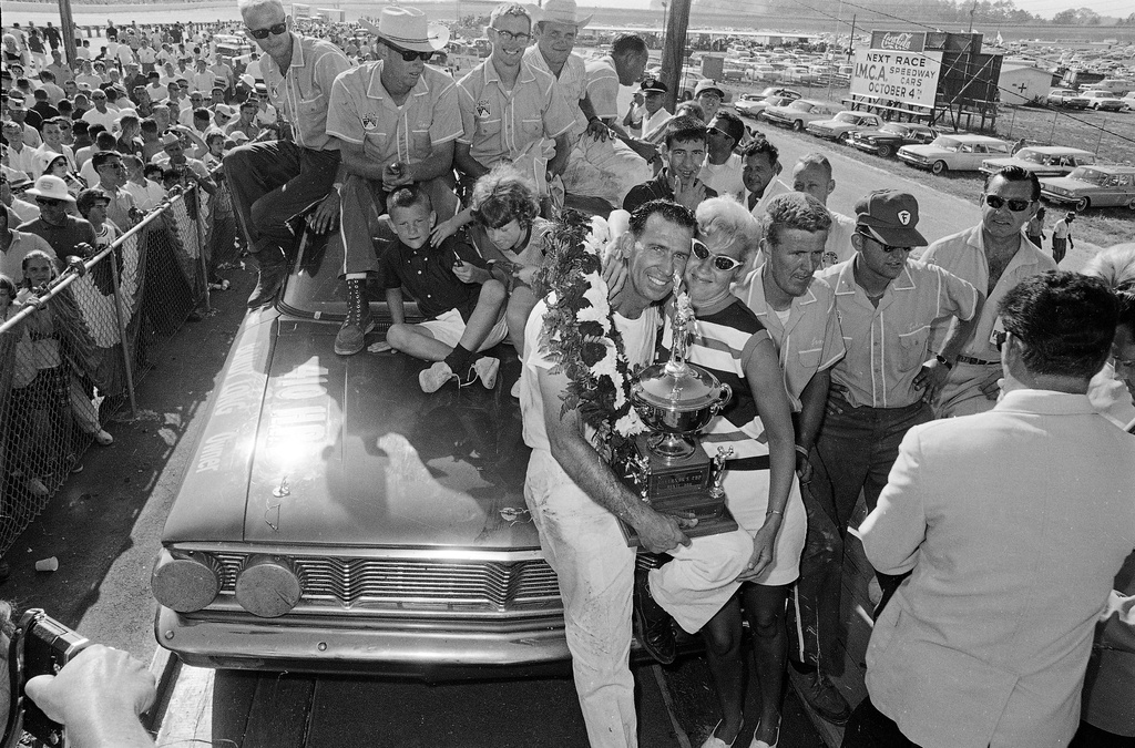 FILE- Ned Jarrett holds his trophy, The Governor's Cup, as he receives a hug from his wife after winning the Dixie 400 stock car auto race June 8, 1964 in Atlanta. (AP Photo/File)