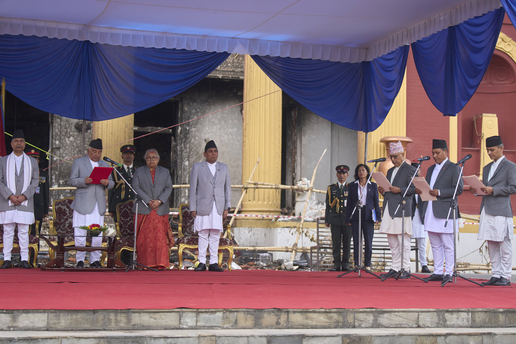 Nepalese President Ram Chandra Poudel, second from left, flanked by new Prime Minister Sushila Karki, third from left, attend an oath swearing ceremony for ministers, right, in front of the presidential building vandalized during recent protests, in Kathmandu, Nepal, Monday, Sept. 15, 2025. (AP Photo/Niranjan Shrestha)